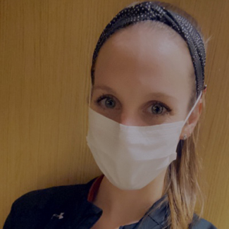Kelly in front of medical equipment wearing a mask
