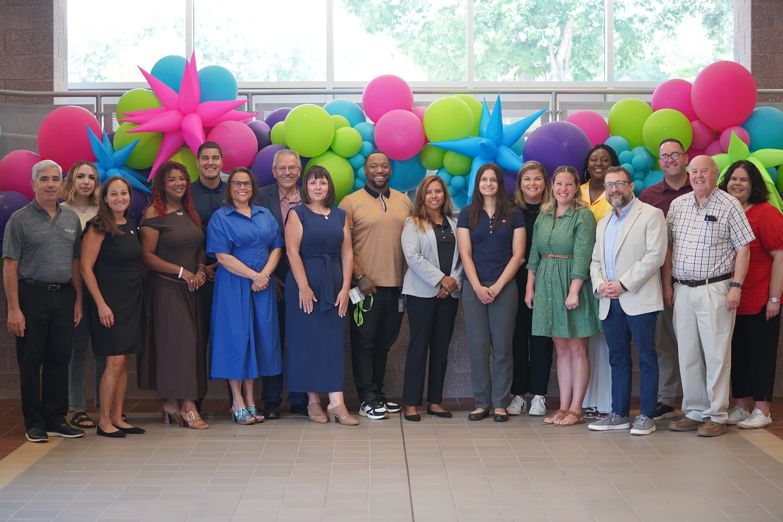 Leadership and staff members stand posed in front of a decorative balloon display.