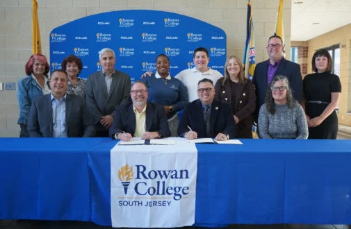 People gathered around a table where two people seated sign a document.