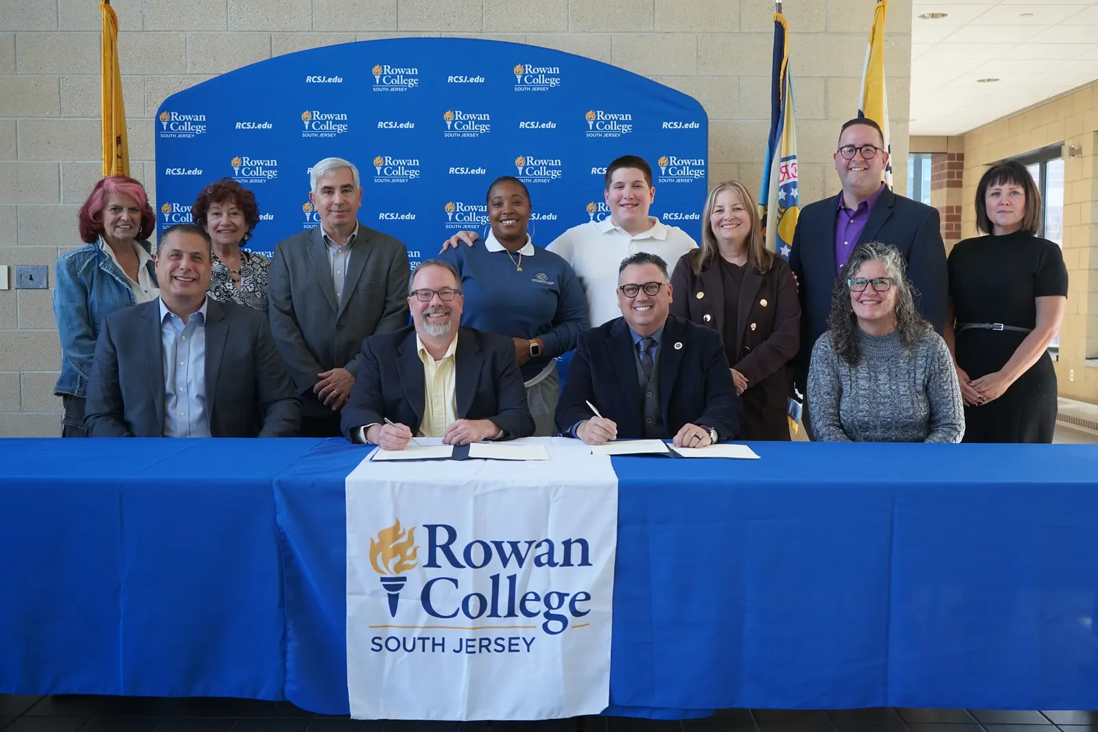 People gathered around a table where two people seated sign a document.