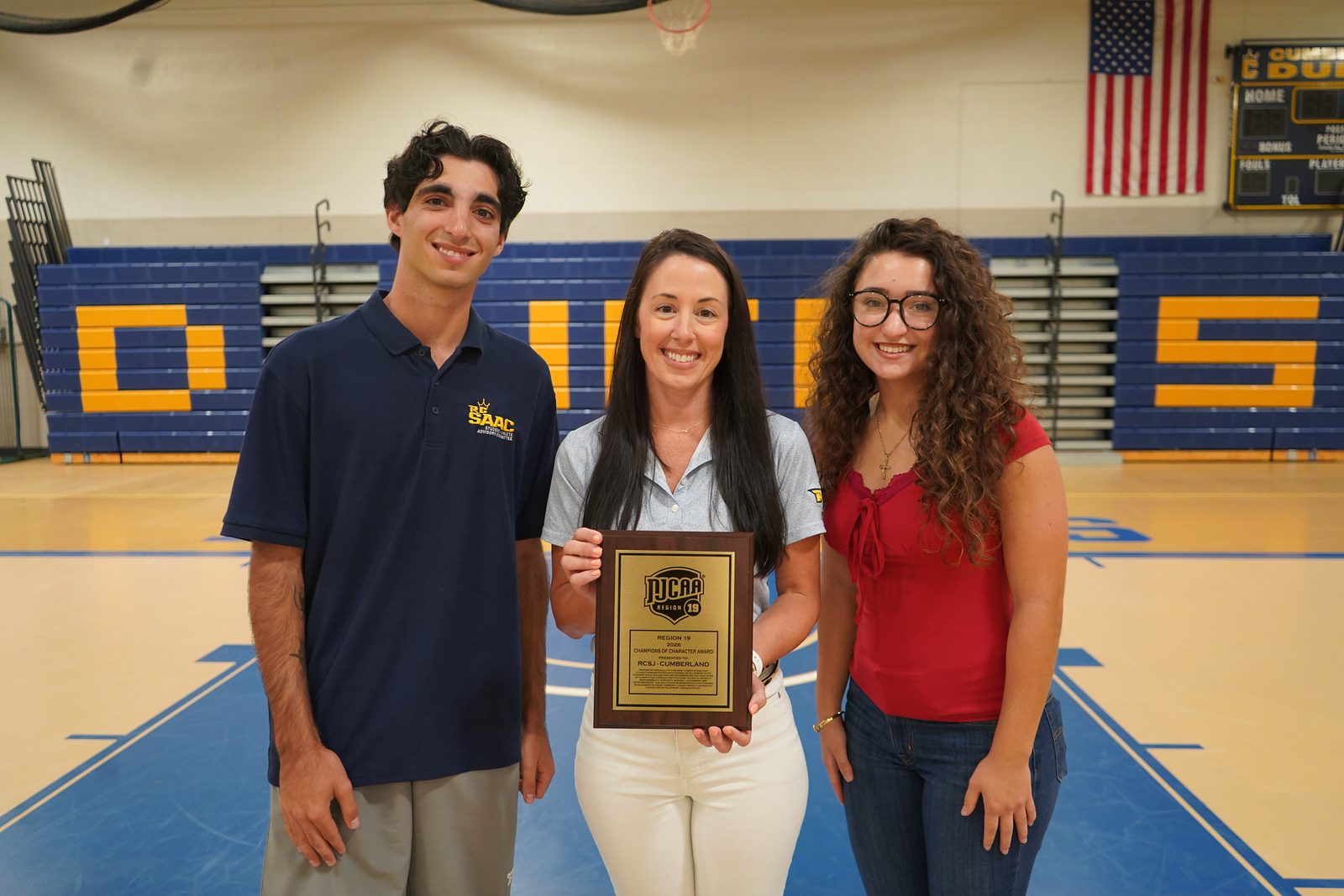 Jeanna DuBois, the RCSJ–Cumberland Dukes assistant athletic director proudly holds the Dukes first-ever Region XIX Champions of Character award. She is surrounded by student-athletes Chris B. and Skylynn O. who are also the president and vice president of the Student-Athlete Advisory Committee.