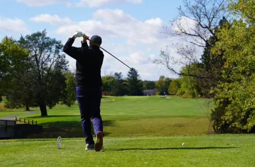 A man standing on a golf course, swinging a golf club.