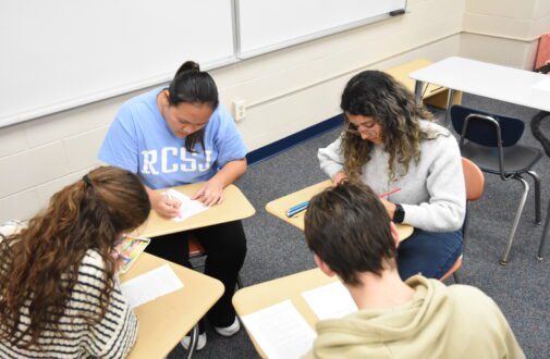 Four students in classroom at desks working.