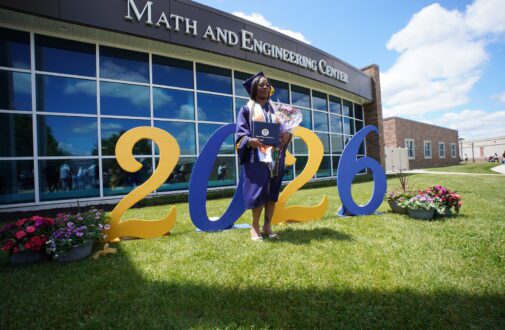 Graduate poses for photo in front of 2026 sign.